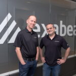 Exabeam CEO Michael DeCesare (L) and chairman and co-founder Nir Polak (R) pose in front of the Exabeam logo in Foster City, California, U.S. in this undated May 2021 handout photograph. Courtesy BIGSHOT PHOTOGRAPHY/Handout via REUTERS.